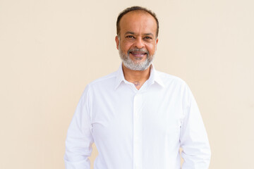 Fototapeta premium Portrait of happy bearded Indian man smiling against plain wall