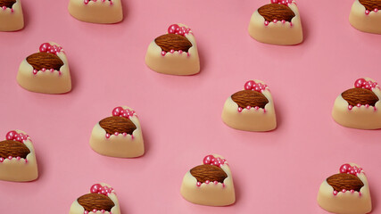 White chocolate candies with almonds in row. Heart shaped sweets. Handmade sweets on a pink background