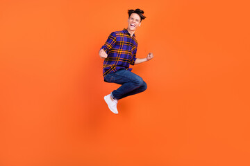 Fototapeta na wymiar Full size photo of millennial hooray guy jump wear shirt jeans sneakers isolated on orange background
