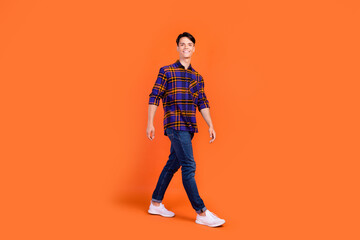 Photo of pretty sweet teenager man dressed checkered clothes walking smiling isolated orange color background