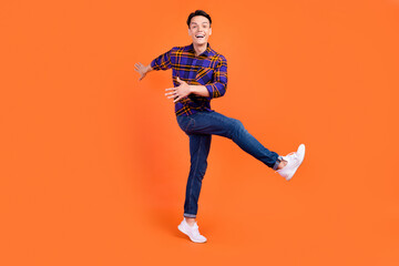 Photo of funny pretty teenager man dressed checkered clothes dancing smiling isolated orange color background