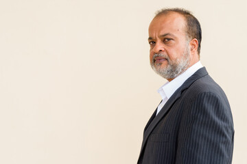 Portrait of handsome bearded Indian man against plain wall