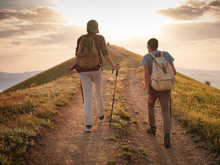 A couple of happy young hikers backpacking on a beautiful rocky trail on a warm, sunset evening. The concept of family travel and adventure. view from behind. Travel lifestyle. © Seleznov_Molchanova