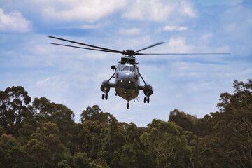 Closeup of a blue helicopter flying in the air on cloudy sky background above the forest
