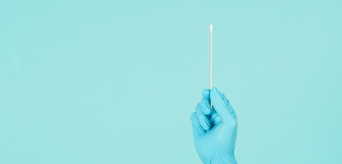 One Cotton stick for swab test in hand with blue medical gloves or latex glove on mint green or...