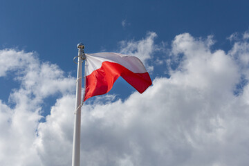 Polish national flag and blue spring sky. National symbol of Poland on the mast.