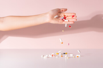 Various pills dropped from female hand on the table. Medicines for headache, colds, high fever, toothache and other diseases. Pink background. Drugs in motion. Refusal of pills concept. Close up.