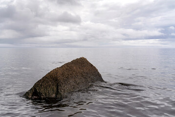 Beautiful autumn misty grey lake with rocky shore and cloudy sky at sunset. Dark and moody nature background. Copy space.