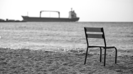 Lonely beach with empty chair and a vessel in the sea on the background. chair on sandy beach at sunset - relaxation concept