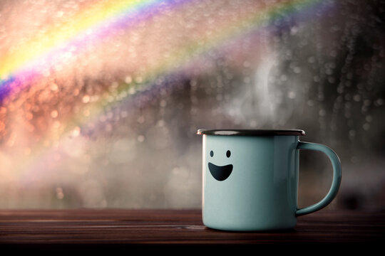 Happiness and Positive Mind, Mental Health Concept. Enjoying Coffee with Smiling Face Cartoon, Blurred Rain with Rainbow as outside view. Smile on Rainy Day