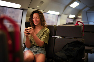 Young beautiful girl tourist travels by train. Happy smiling woman using the phone while travel by train.