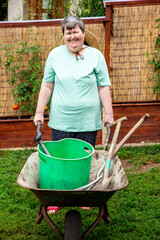 portrait of a mentally handicapped or disabled woman holding a wheelbarrow with gardening tools