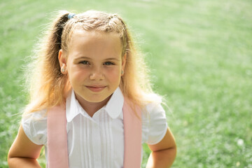 close up portrait of smiling blonde schoolgirl in white shirt with pink backpack back to school outdoor