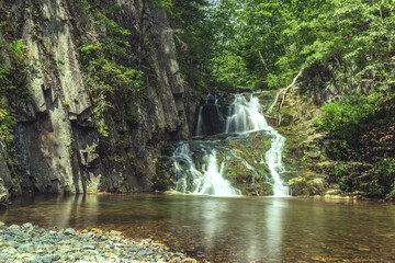 Fototapeta na wymiar A forest waterfall among the volcanic rocks. Summer.