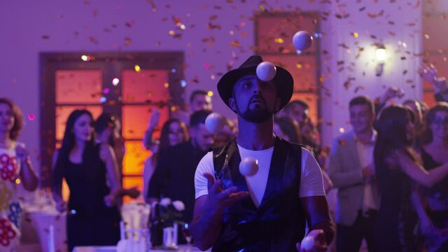 Juggler showing tricks with white balls at colorful party . Man juggling four balls at night party. Many out of focused people in the background . Shot on RED DRAGON Cinema Camera in slow motion.