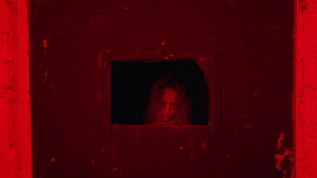 Horror acting - a woman in a straitjacket standing behind the door in mental hospital - getting closer and looking throw the small window