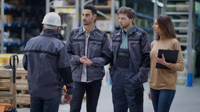Group of employees listening instructions of foreman in warehouse and start working. Experienced professional senior man instructing young Caucasian and Middle Eastern men and woman at workplace