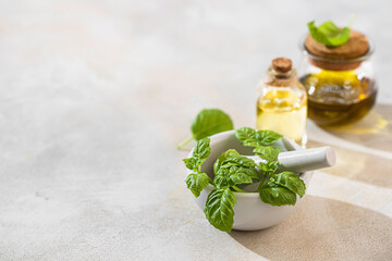 Transparent bottle of basil essential oil, fresh basil leaves in a ceramic mortar with a pestle on...