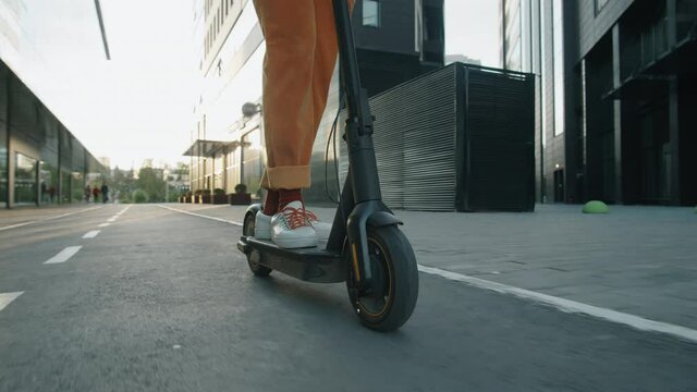 Low section tracking shot of legs of unrecognizable man riding electric scooter on road in city