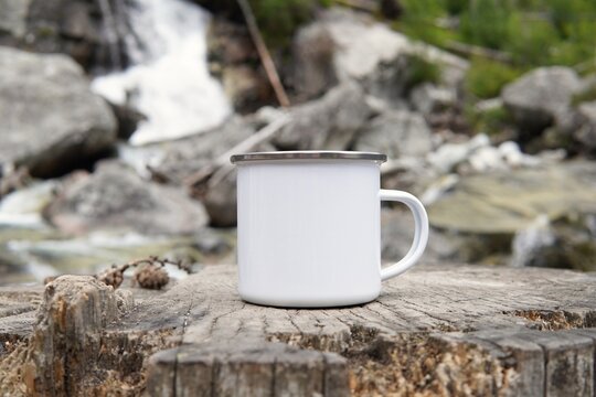 Blank enamel coffee cup mockup, empty camping mug in wild nature for design presentation.