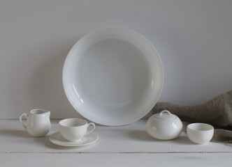 A mock-up of white ceramic dishes on a table against a light wall and gray linen fabric.