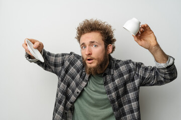 No coffee in inverted cup good looking man with curly hair and beard holding cup, wearing plaid long sleeve shirt isolated on white background. Crisis and lockdown concept.