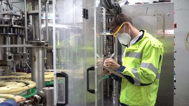 Engineer wearing face mask and protection glasses holding clipboard checking automatic machine in industry manufacturing factory. worker maintenance