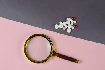 Magnifying glass and medical pills on a gray-pink background. A