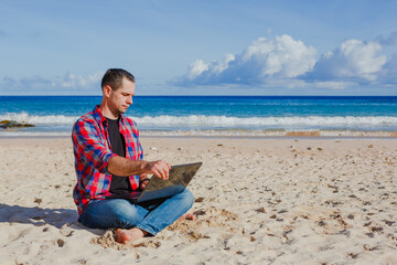 Young man with laptop working on the sand beach