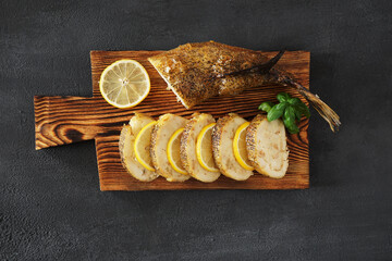  slices of stuffed  fish pike with lemon on a wooden board in the centre on a dark background. top...
