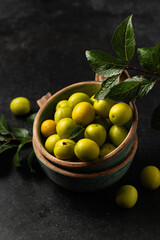 yellow freshly torn cherry plum with green leaves in ceramic cups on a gray background, space for text