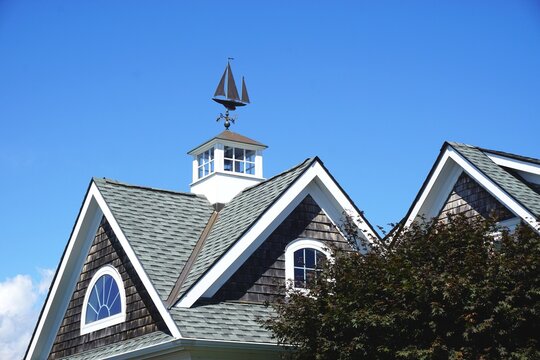 Vintage sailing ship weather vane atop a classic cupola at the peak of a typical New England gable roof with brilliant blue sky