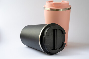 Two thermocups or thermos mugs for tea or coffee against a white background. Black and pink for him and her. Hot beverage for couples