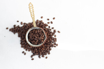 spilled coffee beans and cezve of coffee beans close up on a white background