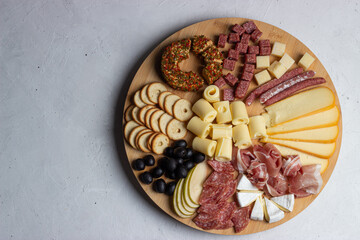 Charcuterie board with selection of meat and cheese served on a wooden round plate on a white...