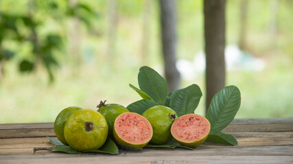 red pulp guavas on wooden table decorated with green leaves outdoors with blurred background