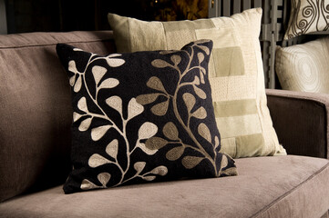 Two pillows with foliage and patchwork pattern on a gray couch