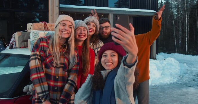 New Year vacation time. Group of happy smiling multiethnic friends take selfie photo at snowy house terrace slow motion.
