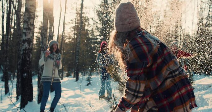 Happy diverse friends enjoy fun snowball fight at sunny winter forest with dog on New Year vacation together slow motion