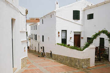 Fototapeta na wymiar View of the alleys and street white architecture and buildings of the town of Es Mercadal, Menorca, Spain during summer season. Empty street with nobody