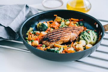 Grilled turkey steak fillet and fried vegetables mix in a black pan on the white table. 