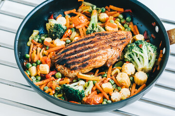 Grilled turkey steak fillet and fried vegetables mix in a black pan on the white table. 