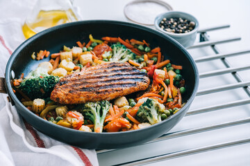 Grilled turkey steak fillet and fried vegetables mix in a black pan on the white table. 