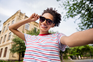 Photo portrait curly girl wearing sunglass striped t-shirt taking selfie outside in summer
