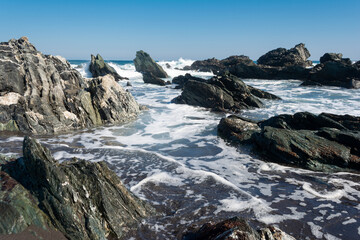 Olas y espuma entre rocas a orilla del mar