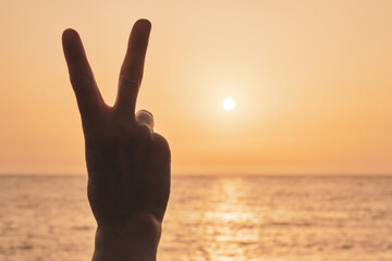 Victory gesture in hand with sun and sea in the background