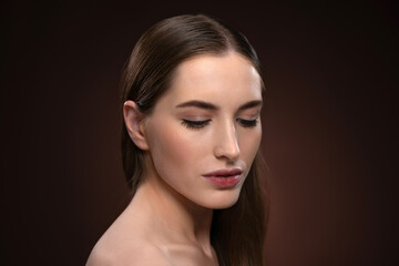 Fototapeta premium Strong and lowered gaze close up portrait with no make up. Healthy pure skin model isolated on black background. Natural make up concept. Spa and beautiful concept. 