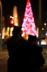 dos chicas abrazadas de espaldas viendo el árbol de navidad iluminado por la noche