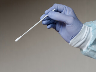 Hand in medical gloves holding an oral sample swab for covid test