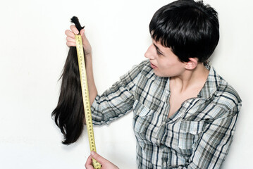 Mujer joven con pelo corto sosteniendo su cabello cortado en una cola de caballo. Medición de la largura del pelo con una cinta métrica. Concepto de donación de cabello para pacientes con cáncer. - obrazy, fototapety, plakaty